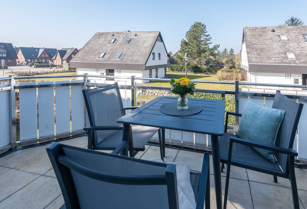 auf dem Westbalkon von Ferienwohnung Carmen App. 12 stehen drei Stühle und ein Tisch mit Blumen