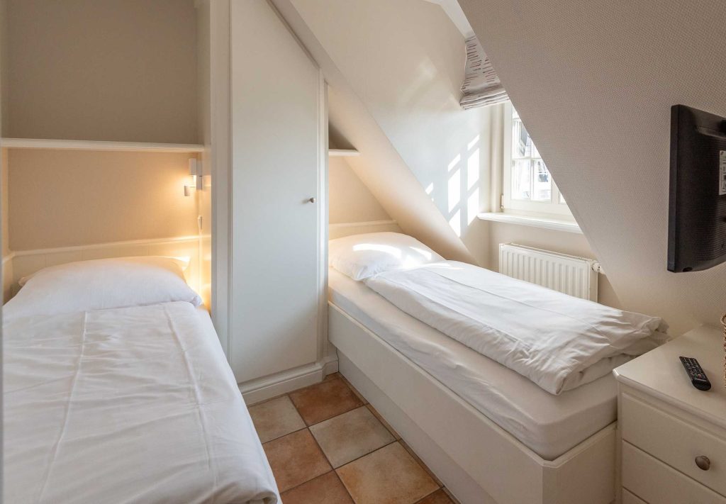 im ersten Schlafzimmer im Haus Carmen App. 12 in Wenningstedt stehen zwei Einzelbetten, ein TV und es gibt ein Fenster