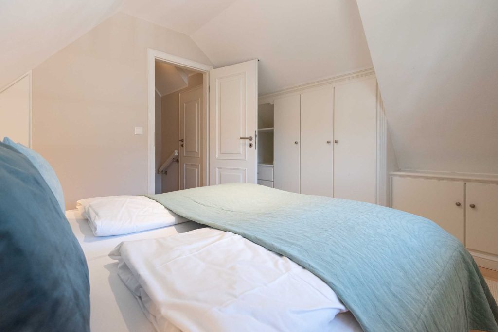 das Doppelbett im Schlafzimmer von App. 12 in Haus Carmen ist mit einer Tagesdecke teilweise abgedeckt