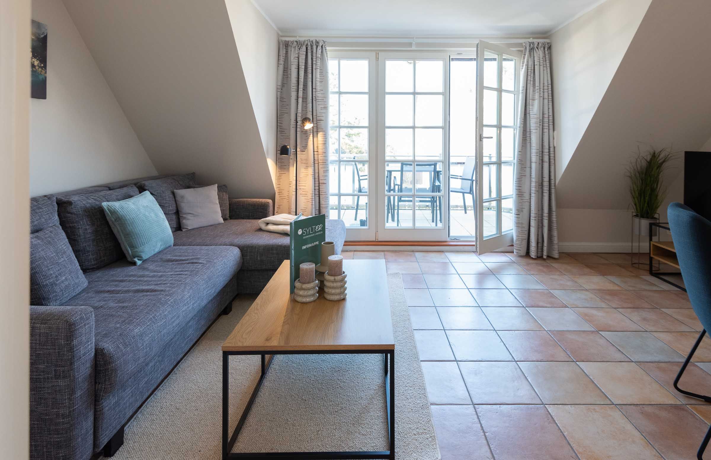im Wohnzimmer von Ferienwohnung Carmen App. 12 steht ein Sofa, Sofatisch und die Balkontür ist offen