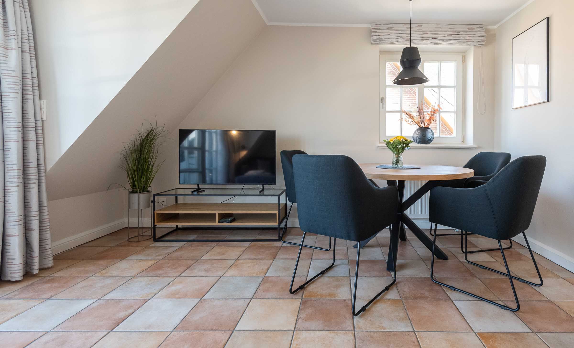 im Wohnzimmer der Ferienwohnung Carmen App. 12 steht ein runder Tisch mit vier Stühlen und links ein TV Board